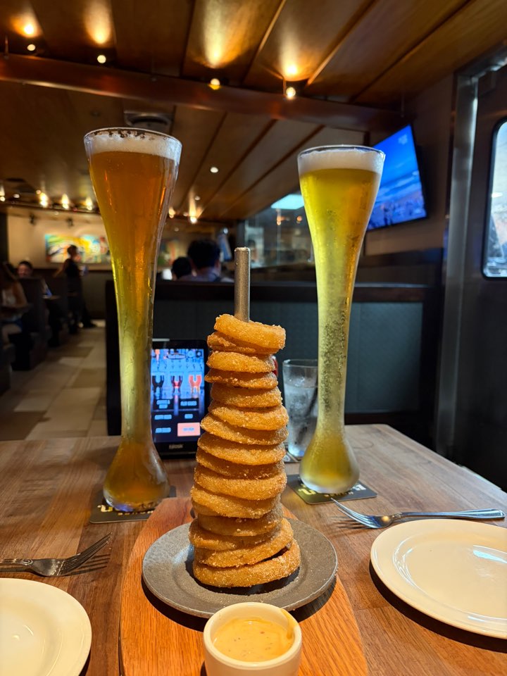 꼬치에 쌓아 올린 어니언 링 타워와 생맥주 두 잔
