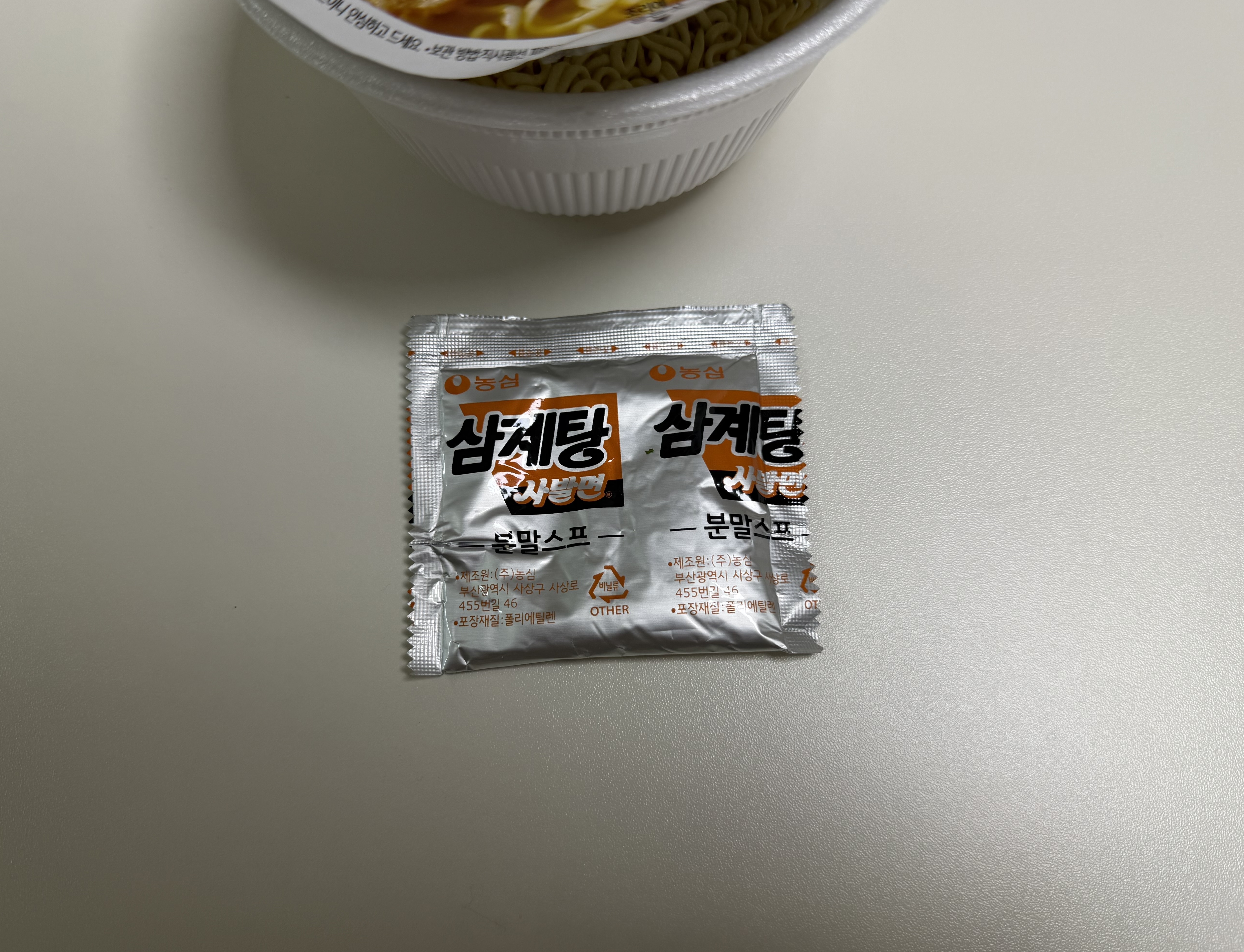 분말스프 봉지 삼계탕 사발면 분말스프 봉지, 은색 포장에 삼계탕 사발면 로고와 제조원 정보가 인쇄되어 있다